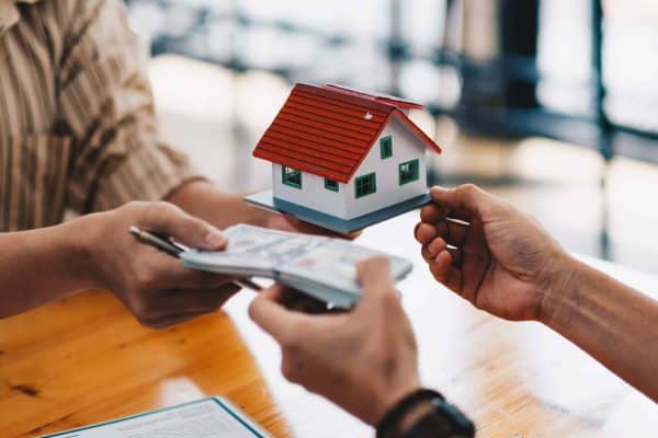 Close up of hands giving house model to other hands with money. Concept of real estate and deal