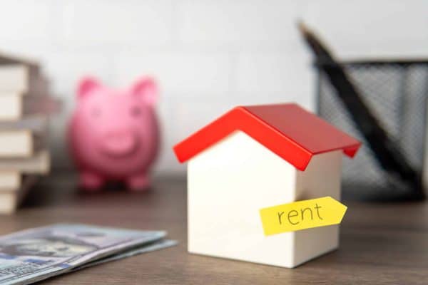 A small toy house with a yellow sticky note labeled "rent" attached to it. Renting property concept.